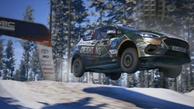 EA Sports WRC – snímek obrazovky zobrazující M-Sport Poland Fiesta Rally3 Williama Creightona, jak se vznáší ve vzduchu v zasněženém lese