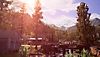 Life Is Strange True Colors-skærmbillede, der viser en smuk lille by med en bro henover en lille flod. Bjerge kan ses i horisonten
