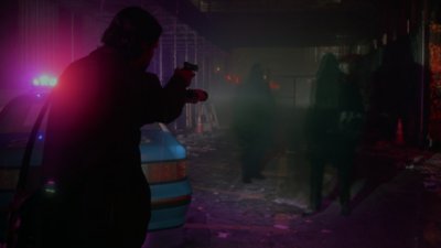 Alan Wake 2 – Screenshot von Alan, der eine Waffe hält und seine Taschenlampe auf mehrere schattenhafte Gestalten richtet