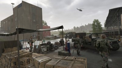 《Arma Reforger》螢幕截圖，呈現建築物之間的前哨基地，士兵站在貨物和載具周圍 