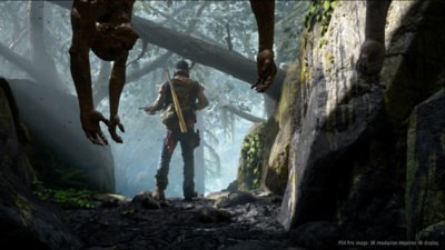 Captura de pantalla de Days Gone con el personaje principal Deacon St. John de pie en un bosque brumoso con cadáveres colgando en primer plano.