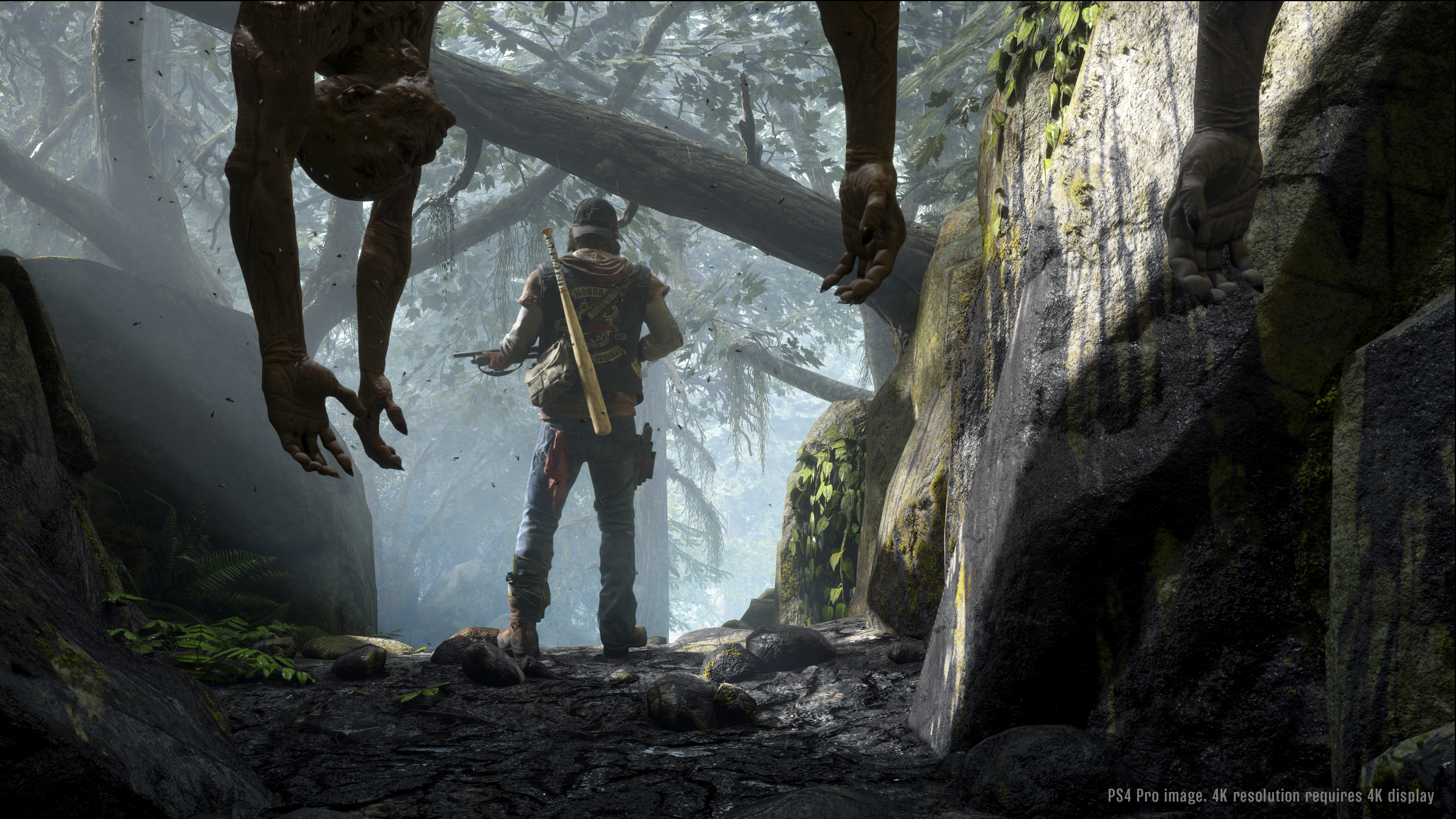Captura de pantalla del juego Days Gone con el personaje principal Deacon St. John de pie en un bosque brumoso con cadáveres colgando en primer plano.