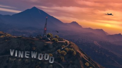 Grand Theft Auto V - Captura de tela mostrando o pôr do sol sobre uma paisagem montanhosa com um letreiro gigante de “Vinewood”