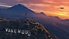 Екранна снимка на Grand Theft Auto V на залязващо слънце над хълмист пейзаж с „Vinewood“, изписано с гигантски букви