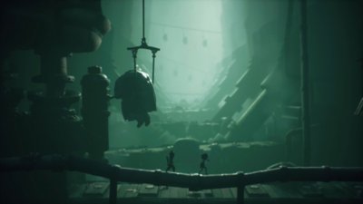 Ein Screenshot aus Little Nightmares 3, der zwei Gestalten zeigt, die in einer Fabrik auf einem Rohr entlanglaufen 
