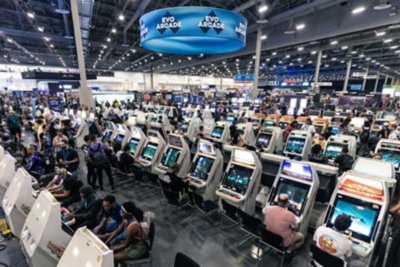 EVO 2024の写真 座って遊ぶタイプのアーケード筐体の列でゲームをプレイする人々。 