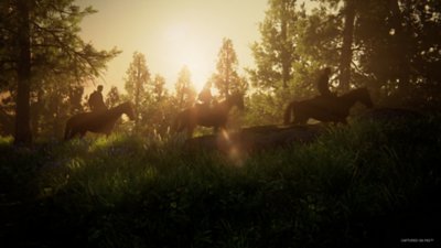 Captura de pantalla del juego The Last of Us Parte I que muestra a tres personas montando a caballo por un bosque con una hermosa puesta de sol de fondo