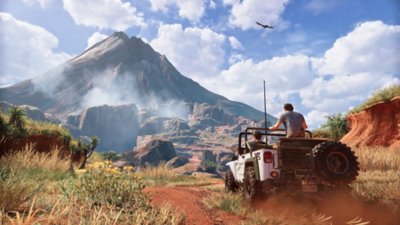لقطة شاشة من Uncharted 4 تعرض "ناثان" و"سام" يقودان سيارة jeep بيضاء على التراب باتجاه بركان بعيد